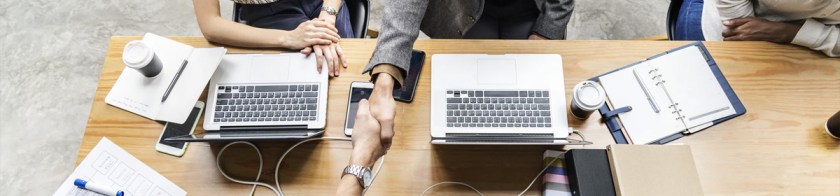 Handshake across a table with computers